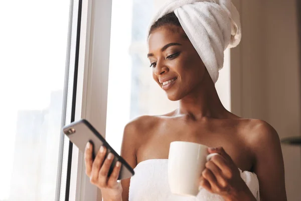 Bela Mulher Africana Envolta Uma Toalha Usando Telefone Celular Enquanto — Fotografia de Stock