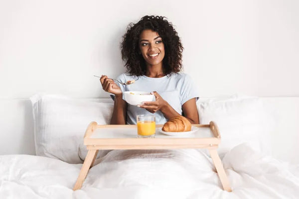 微笑的年轻非洲妇女有美味的早餐托盘在床上 — 图库照片