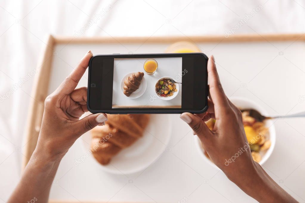 Close up of an african woman taking a picture of her breakfast in bed
