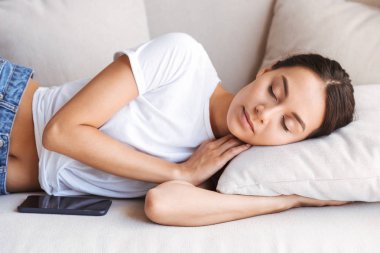 Genç ve güzel Asyalı kadın cep telefonu evde kanepede yatıyor