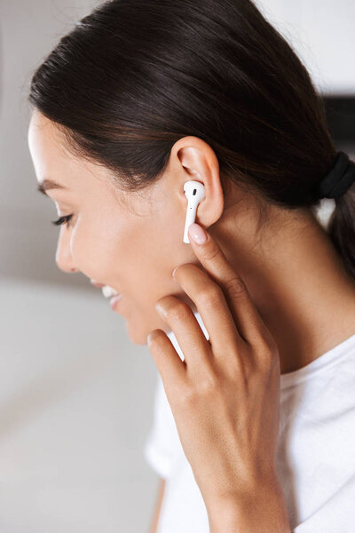 Крупный план улыбающейся азиатской женщины, слушающей музыку в помещении с наушниками
