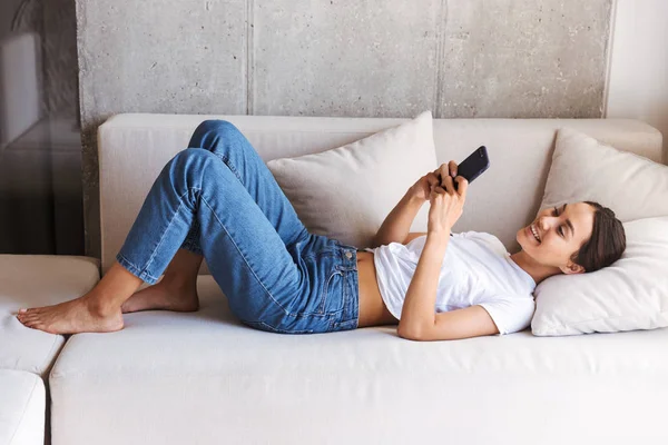 幸せな若いアジア女性 自宅でソファの上に敷設しながら携帯電話を使用して — ストック写真