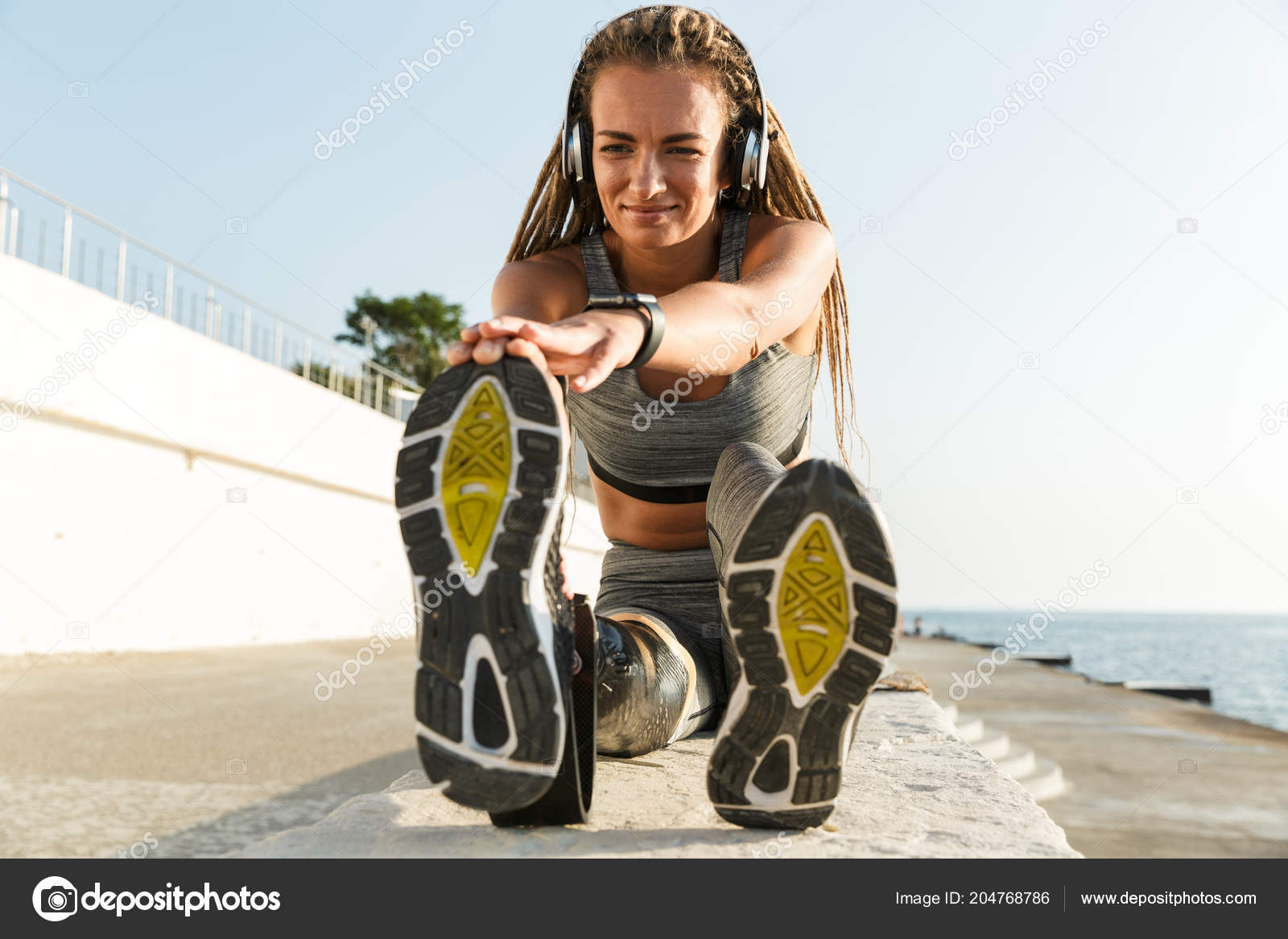 Smiling sportswoman with prosthetic leg wearing headphones sitting
