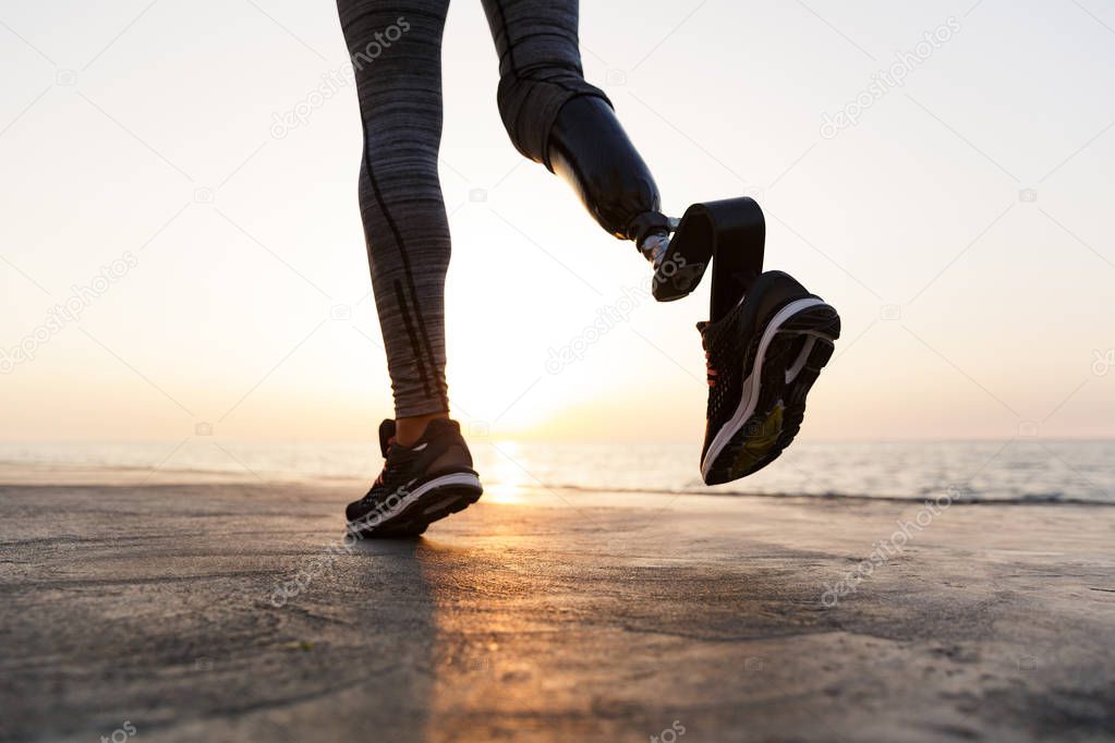 Close up of disabled woman with prosthetic leg running outdoor at the beach