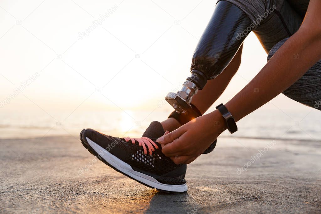 Close up of athlete woman with prosthetic leg tying shoelace outdoor at the beach