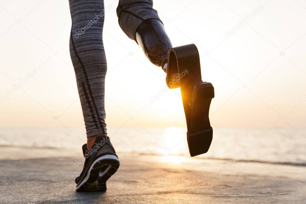 Close up of disabled athlete woman with prosthetic leg running outdoor at the beach