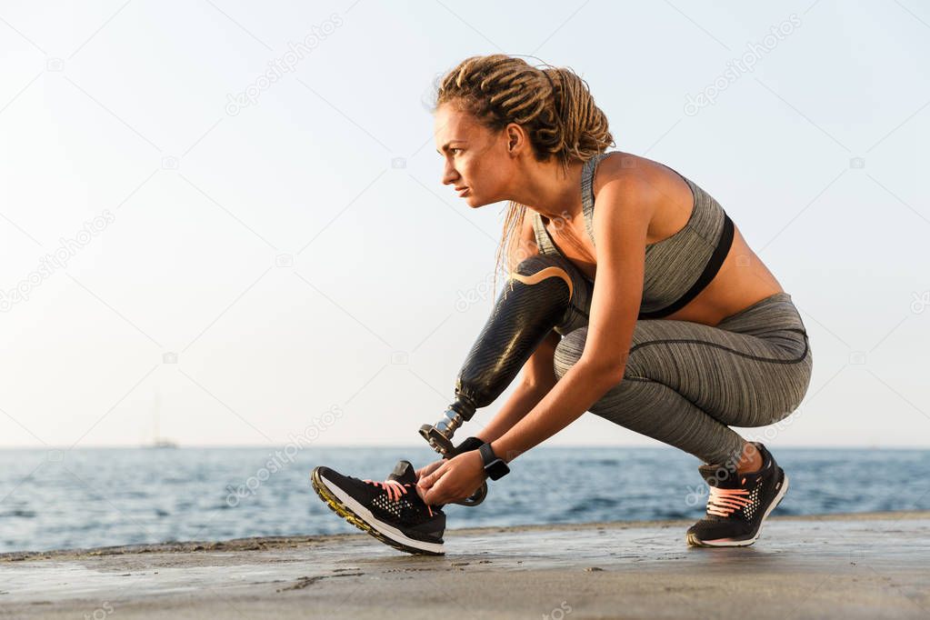 Confident disabled athlete woman with prosthetic leg tying shoelace outdoor