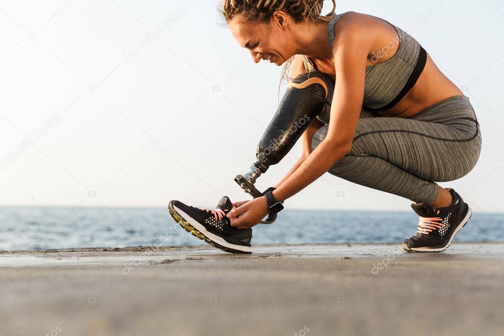 Smiling disabled athlete woman with prosthetic leg tying shoelace outdoor