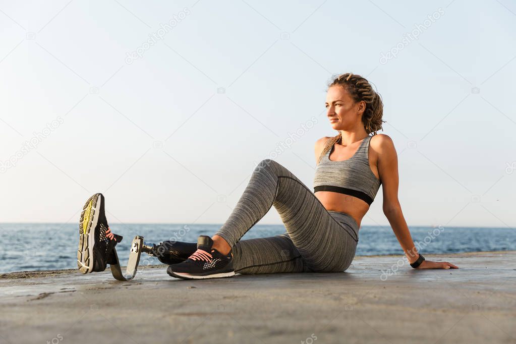 Image of young amazing disabled sports woman sitting on the beach resting outdoors.