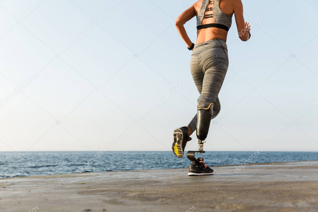 Cropped back view of young amazing disabled sports woman running on the beach outdoors.