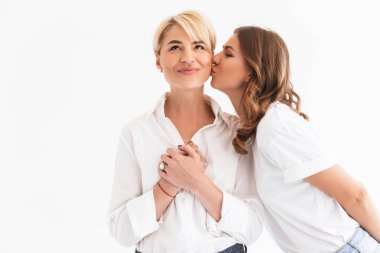 Portre closeup iki neşeli güzel kadınlar, genç kızı güzel annesi beyaz arka plan üzerinde izole ayakta yanağından öpmek