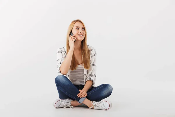 快乐的年轻休闲女孩的肖像坐在与腿交叉孤立的白色背景下的手机交谈 — 图库照片
