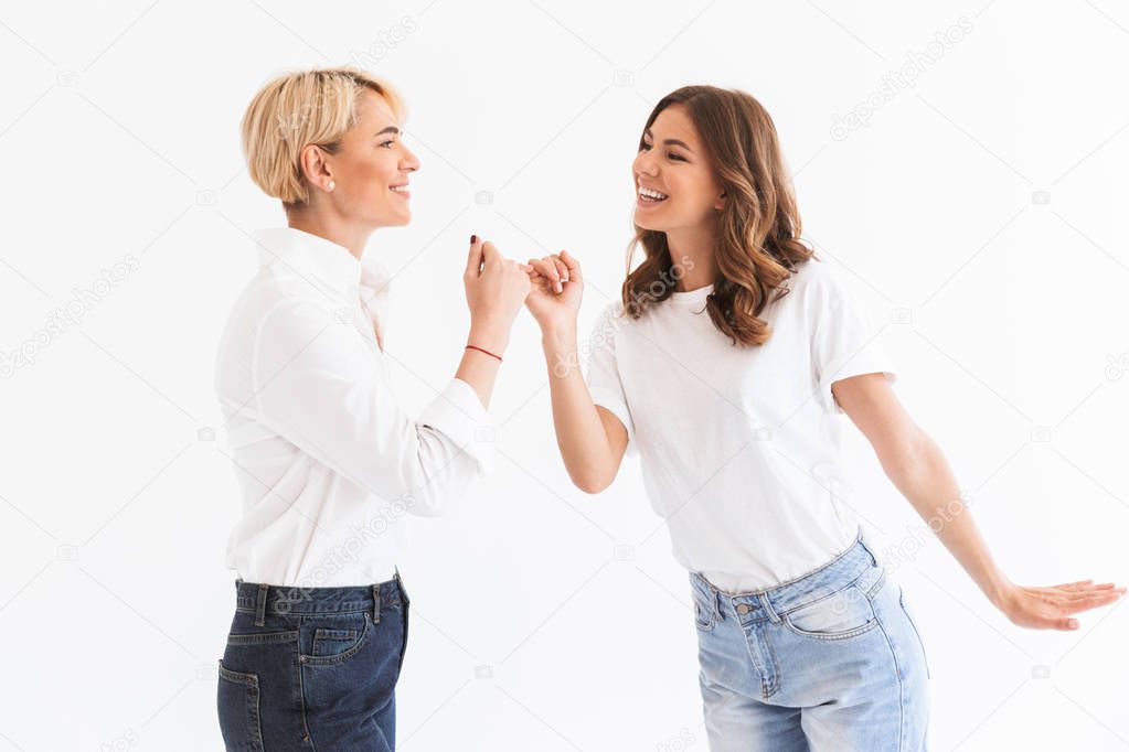 Photo of lovely family mother 40s and daughter 16-18 hooking each other's little fingers in conciliation or friendship standing isolated over white background