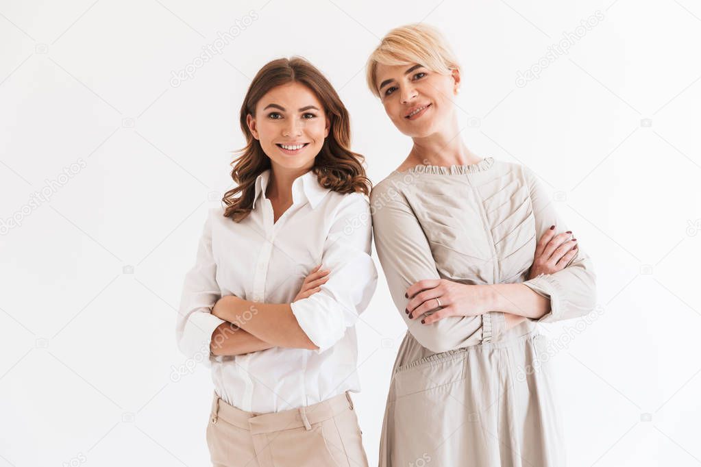 Photo of two beautiful women mother and daughter standing together with arms folded isolated over white background