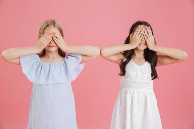 Eğleniyor ve pembe arka plan üzerinde izole elleriyle gözlerini kapsayan fotoğraf eğlenceli küçük kızlar 8-10 yaşında giyen elbiseler