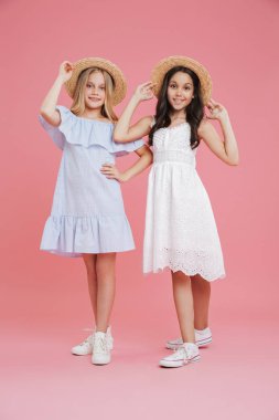 Güzel yaz kızlar 8-10 giyen tam uzunlukta portre üzerinde pembe arka plan izole gülümseme ile hasır şapkalar dokunmadan kamera poz Giydir