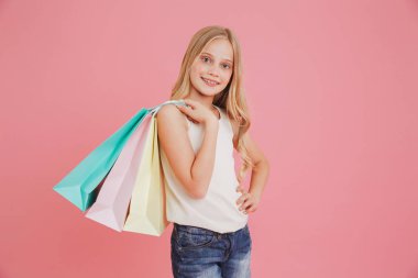 Sarışın beyaz kız 8-10 kameraya gülümseyen ve renkli alışveriş torbaları üzerinde pembe arka plan izole alımları ile tutarak casual giyim