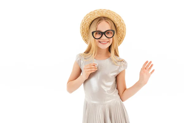 ドレスと白い背景の上にカメラを見ながら偽眼鏡でポーズ麦わら帽子で幸せな若いブロンドの女の子 — ストック写真