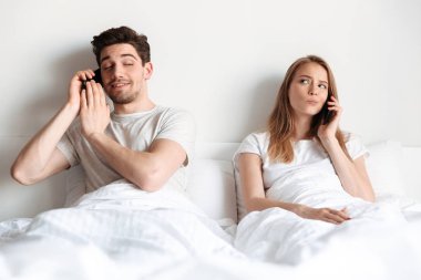 Genç sevgili çift bir kenara bakarak akıllı telefonlar tarafından söz yatakta yatıyor.