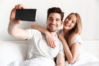 Sevgi dolu çift yatakta yatıyor genç görüntüsünü almak bir selfie bir kenara seyir smartphone tarafından.