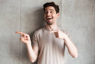 Heyecanlı gülümseyen genç adam bir kenara boşaltmak için işaret eden arka plan gri duvar bakmaktan ayakta fotoğrafı.