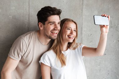 İki mutlu insanlar erkek ve kadın selfie smartphone beton gri duvar üzerinde kapalı izole kamera gülüp fotoğrafta görüntü