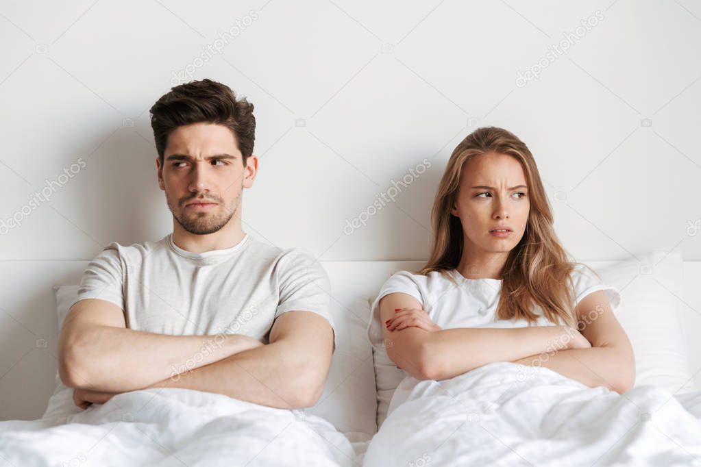 Image of young displeased negative offended loving couple lies in bed quarrel.