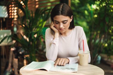 Bir kafede otururken açık havada bir smoothies ile dergi okuma dalgın genç kız