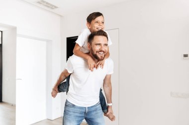 Neşeli mutlu baba beyaz parlak evinde istirahat ederken beyaz çocuk 8-10 piggybacking görüntüsünü