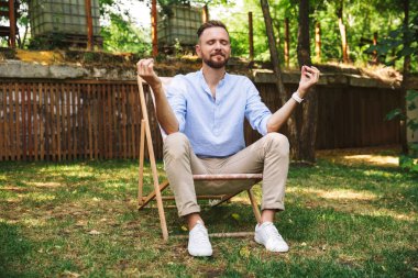 Fotoğrafı rahat yakışıklı 30'lu Salon Başkanı kapalı gözler ve yoga hareketi ile yeşil park içinde kalan sırasında oturan adam