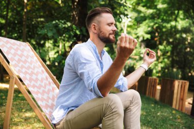 Portre rahat beyaz adam şezlong kapalı gözler ve yoga hareketi ile yeşil park içinde kalan sırasında oturan 30'lu