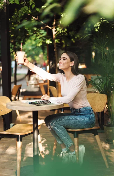 一个开朗的女孩捧着一杯冰沙 而坐在户外咖啡馆 — 图库照片