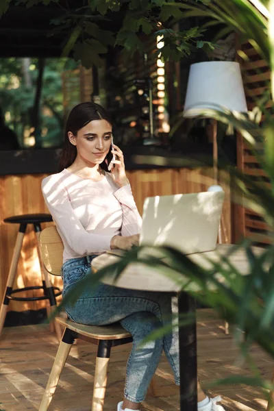 Mosolygó Fiatal Lány Beszél Mobiltelefonon Miközben Kávézó Asztal Laptop Számítógéppel — Stock Fotó