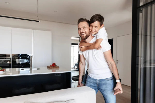 Imagen Hombre Sonriente Satisfecho Cuestas Hijo Mientras Divierte Moderno Apartamento — Foto de Stock