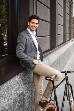 Genç işadamı açık havada bir bisiklet ile ayakta iken bir duvara yaslanmış gülümseyen