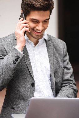 Üstünde hareket eden telefon uymak dizüstü bilgisayar açık havada oturan çalışırken neşeli genç işadamı giymiş