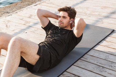 Yakışıklı genç sporcunun fotoğrafı spor egzersizleri açık havada beach kulaklık ile müzik dinleme yapmak.