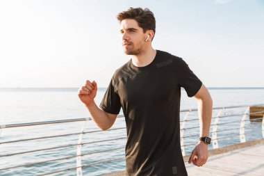 Açık havada beach kulaklık ile müzik dinleme üzerinde çalışan yakışıklı genç sporcu görüntüsünü.