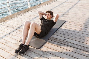 Yakışıklı genç sporcunun fotoğrafı spor egzersizleri açık havada beach kulaklık ile müzik dinleme yapmak.