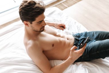 Evde yatakta döşeme sırasında cep telefonu kullanan ciddi gömleksiz adam