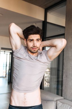 Çekici bir genç adam evde ayakta iken tişörtünü alarak