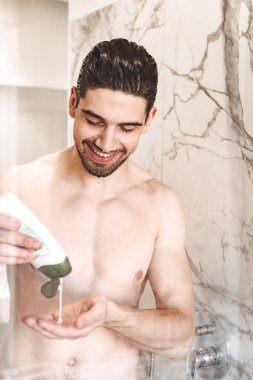 Şampuan şişesi tutan genç çıplak adam hediye, gülümseyen