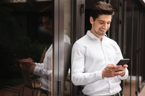 Smiling Young Businessman Using Moible Phone While Standing Glass Doors — Stock Photo, Image