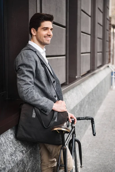 自転車で屋外立ちながら壁に寄りかかって青年実業家を笑顔 — ストック写真