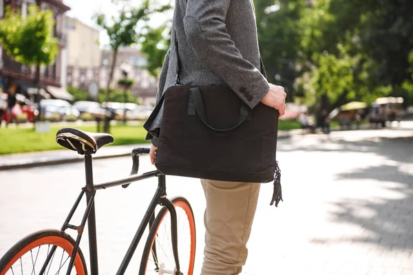 Cropped image of a young businessman with bag standing with a bicycle outdoors