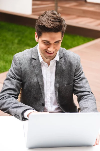 屋外に座ってラップトップ コンピューターで作業してスーツを着て魅力的な青年実業家 — ストック写真