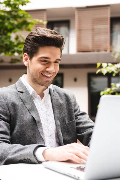 Усміхнений Молодий Бізнесмен Одягнений Костюм Працює Ноутбуці Сидячи Відкритому Повітрі — стокове фото
