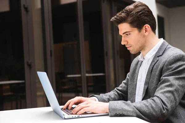 屋外に座ってラップトップ コンピューターで作業服に身を包んだ集中の青年実業家 — ストック写真