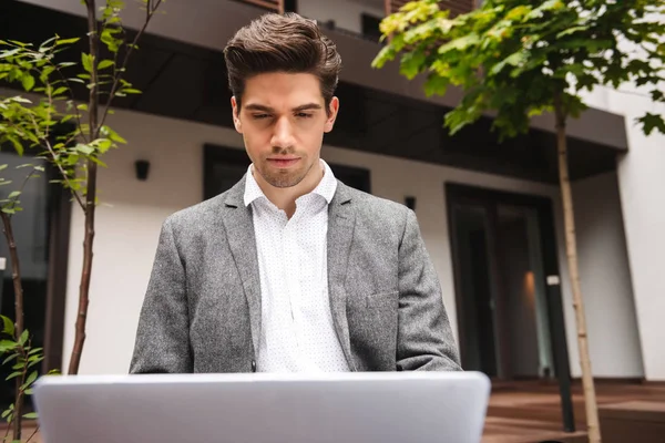 屋外に座ってラップトップ コンピューターで作業してスーツを着て自信を持って若いビジネスマン — ストック写真