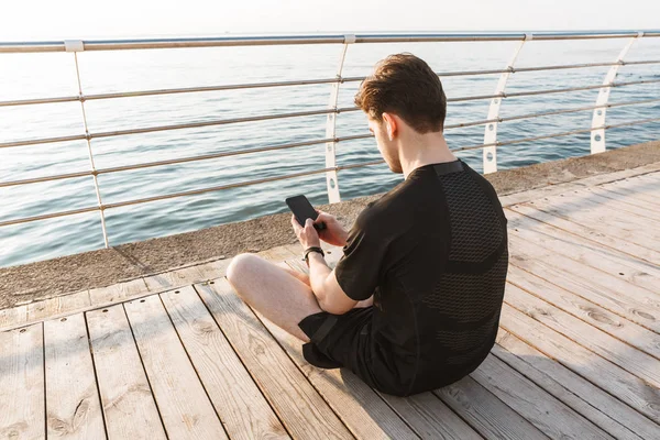 Genç Sporcunun Fotoğrafı Görünümü Açık Havada Cep Telefonuyla Sahilde Geri — Stok fotoğraf